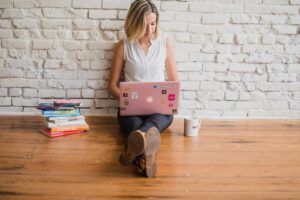 woman sitting with open laptop beside a stack of books