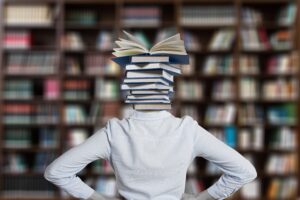 woman with a stack of books instead of a head, facing shelves of books
