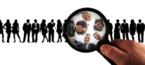 silhouetted people standing in line, with magnifying glass highlighting a few faces