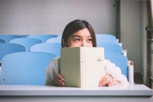 woman in a classroom with her eyes visible over an open book