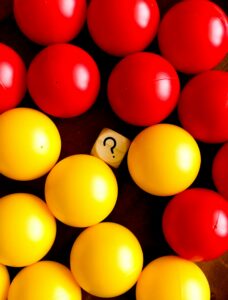 one small wooden die with a question mark surrounded by larger round objects