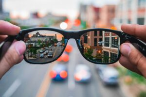 Person holding up eyeglasses. The background is blurred but the part seen through the lenses is clear.