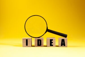 the word "Idea" spelled out in Scrabble tiles with a magnifying glass perched on top