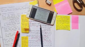 desk with a piece of paper with writing, sticky notes, and a phone with a text on the screen