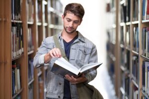 person in library looking at a book while walking through the stacks
